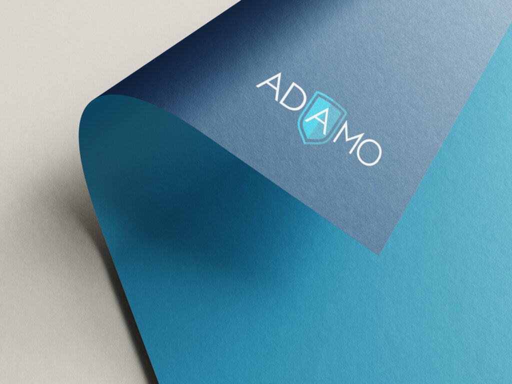 A photo of the rebrand Adamo logo on the corner of a piece of paper