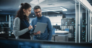 A man and woman in an office look at a laptop together